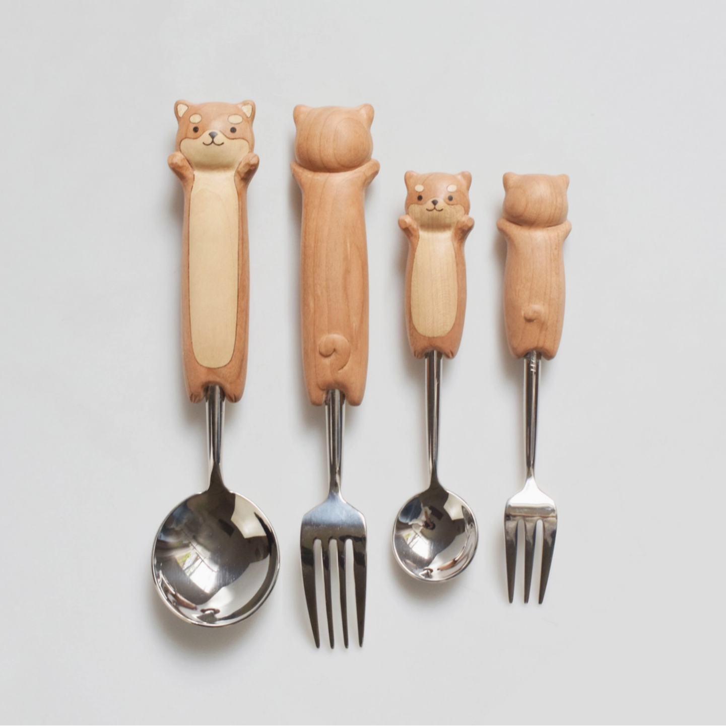Set of four wooden-handled cutlery with dog-shaped handles on a light gray background