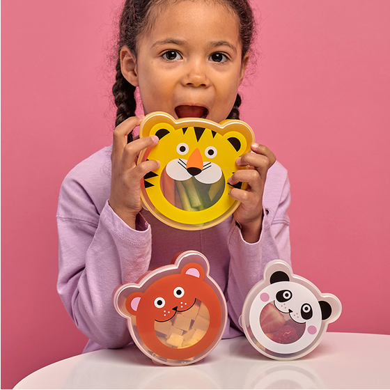 Child holding a tiger-shaped snack box with two other animal boxes on a pink background