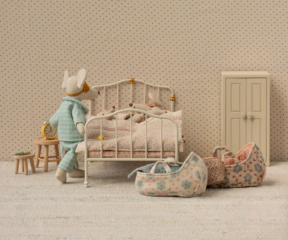 Dollhouse bedroom with a bed, toys, and furniture against a patterned wall.