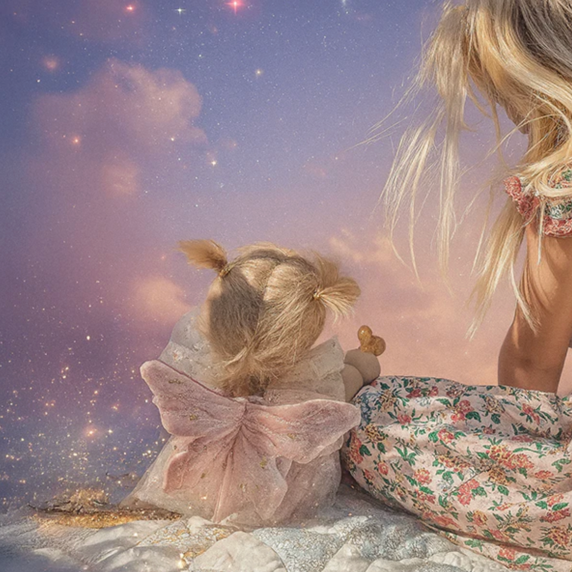 A child and a doll in fairy costumes sitting on a cloud with a starry sky background