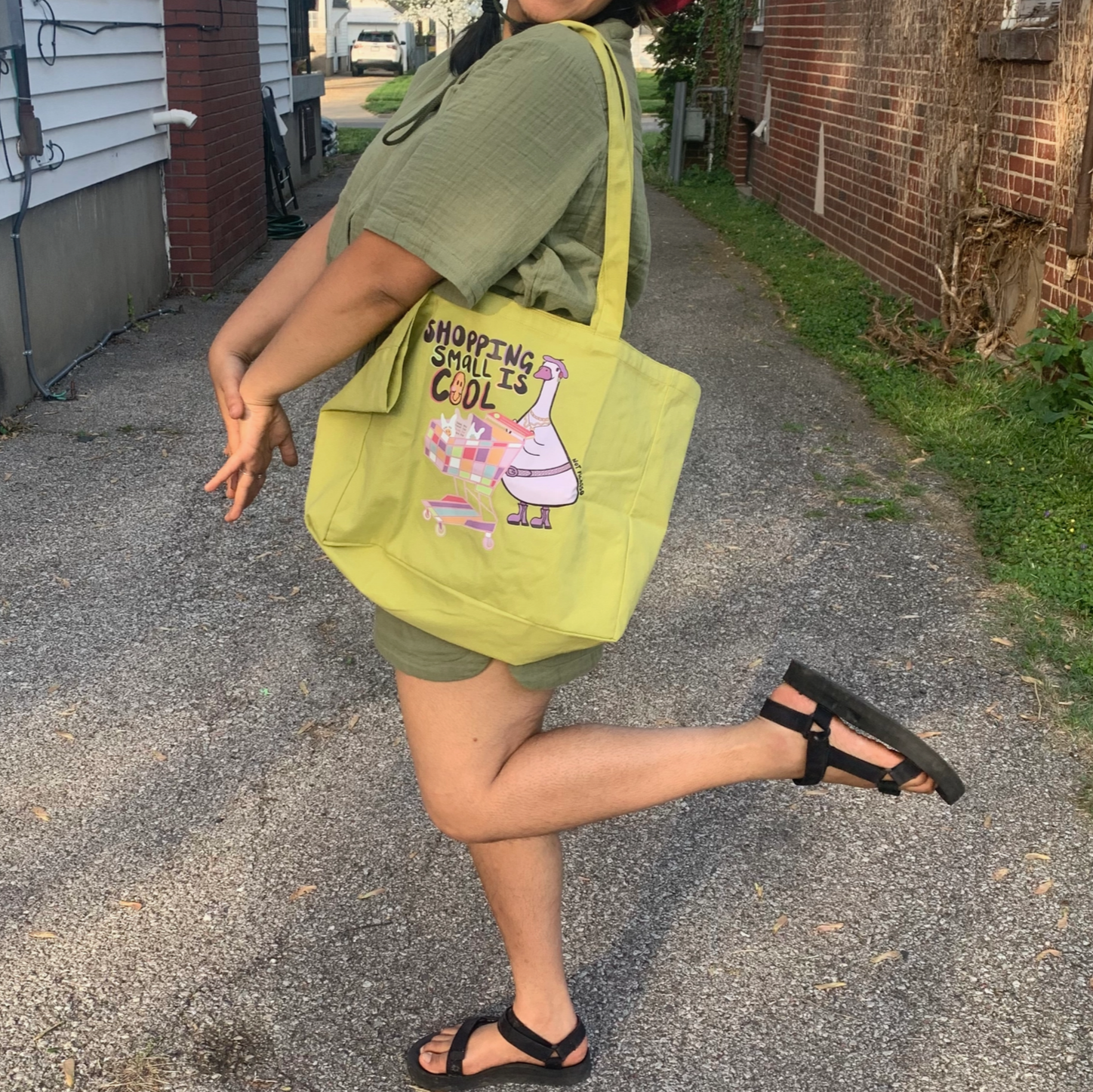 Person walking outdoors with a bright green tote bag featuring a cartoon character.