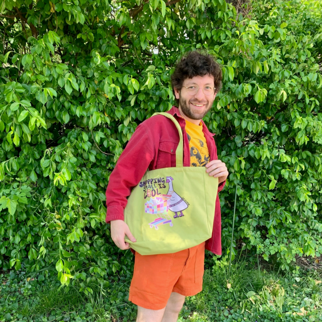 Person holding a green bag with a design, standing in front of green foliage