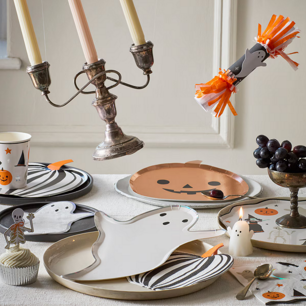 Halloween-themed table setting with ghost plates, jack-o'-lantern plates, and decorative candles.