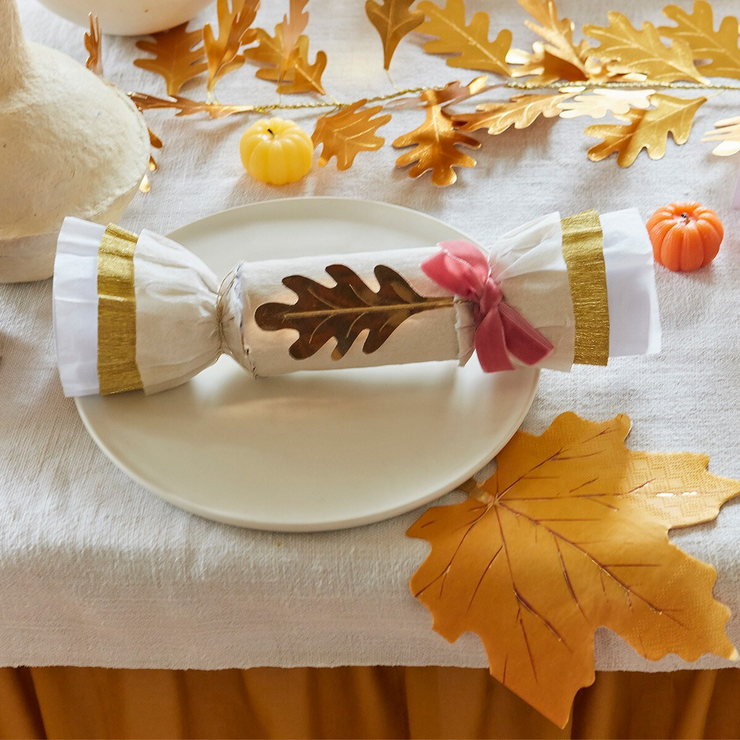Decorative cracker with gold leaf design on a plate with autumn leaves and pumpkins.