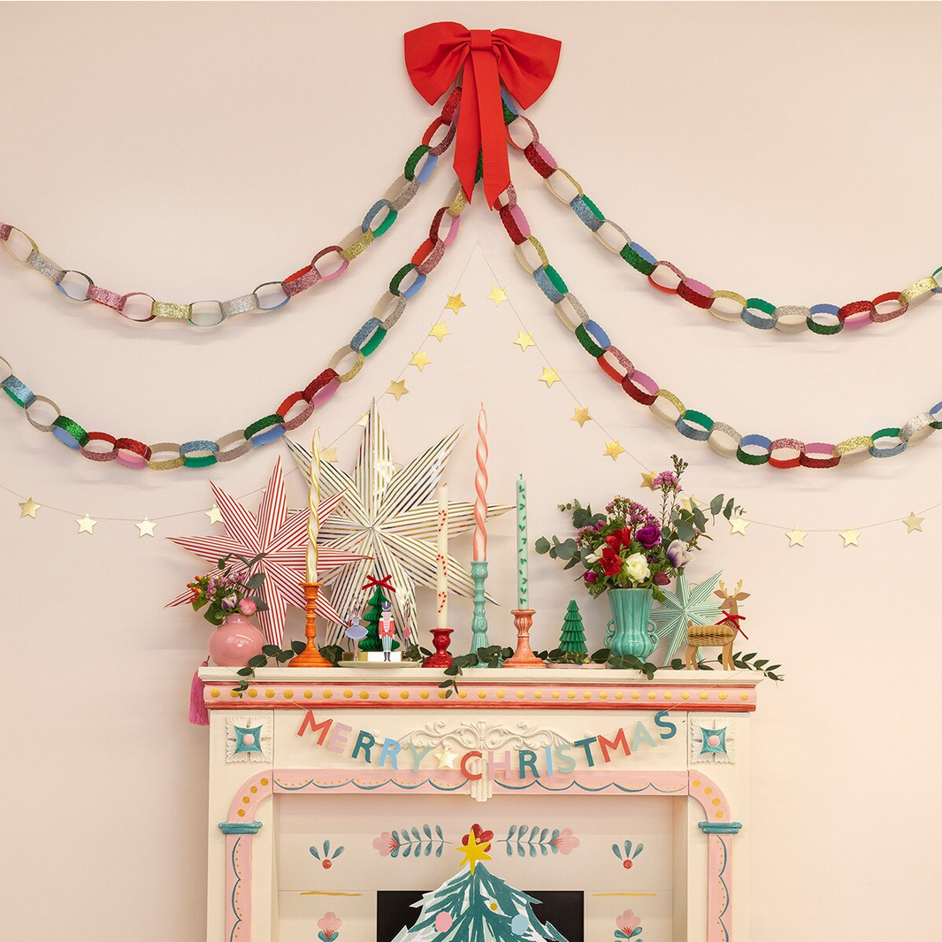 Decorative Christmas mantel with colorful garlands, candles, and a 'Merry Christmas' banner.