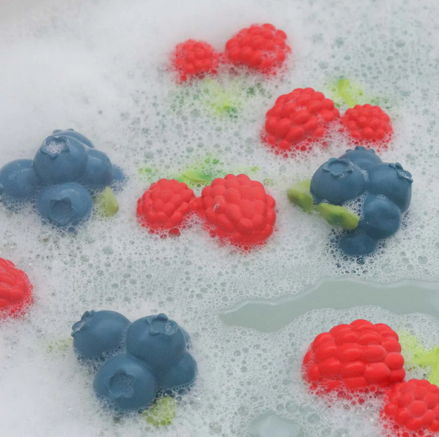 Colorful berry-shaped bath bombs in a soapy water bath.