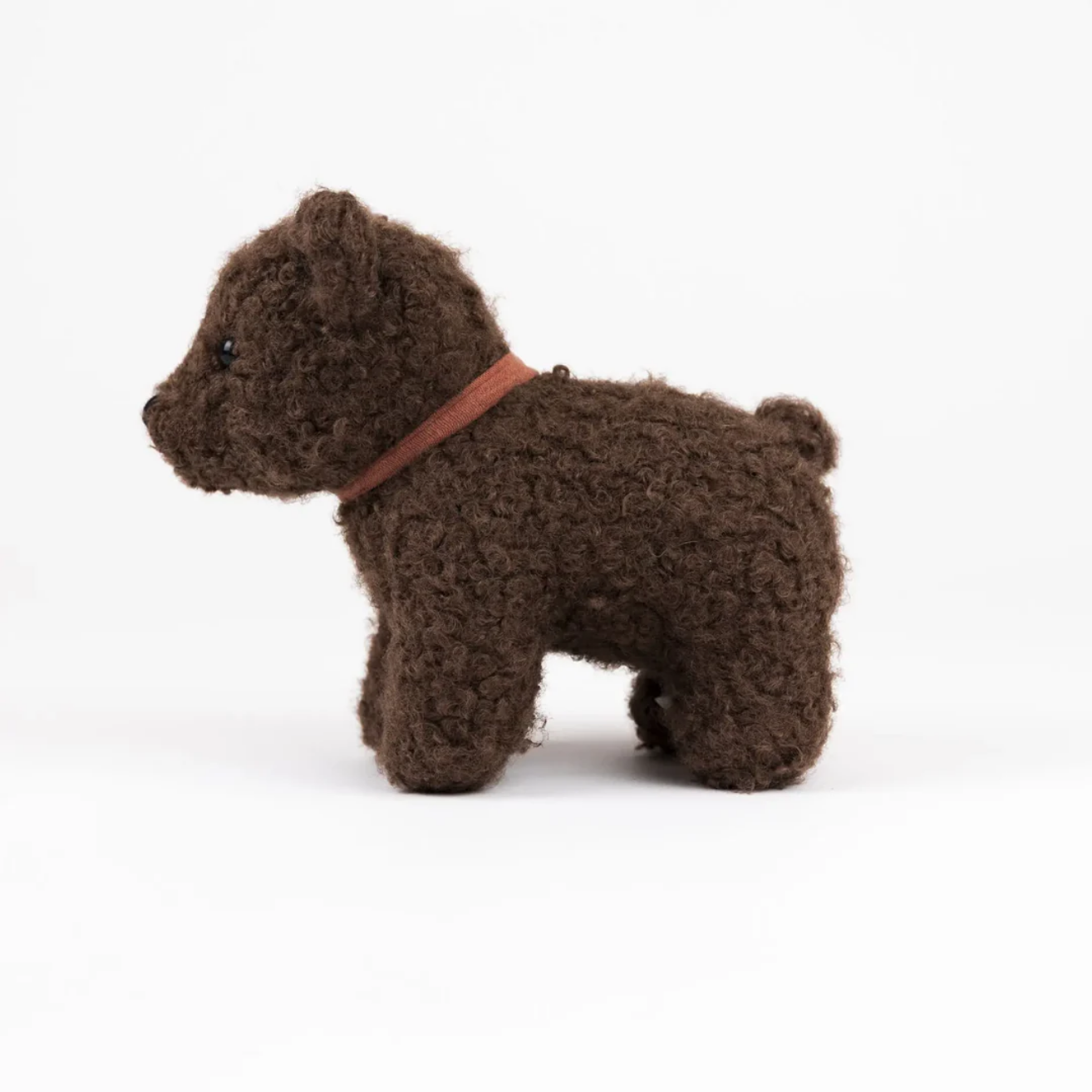 Small brown bear toy with a red collar on a white background