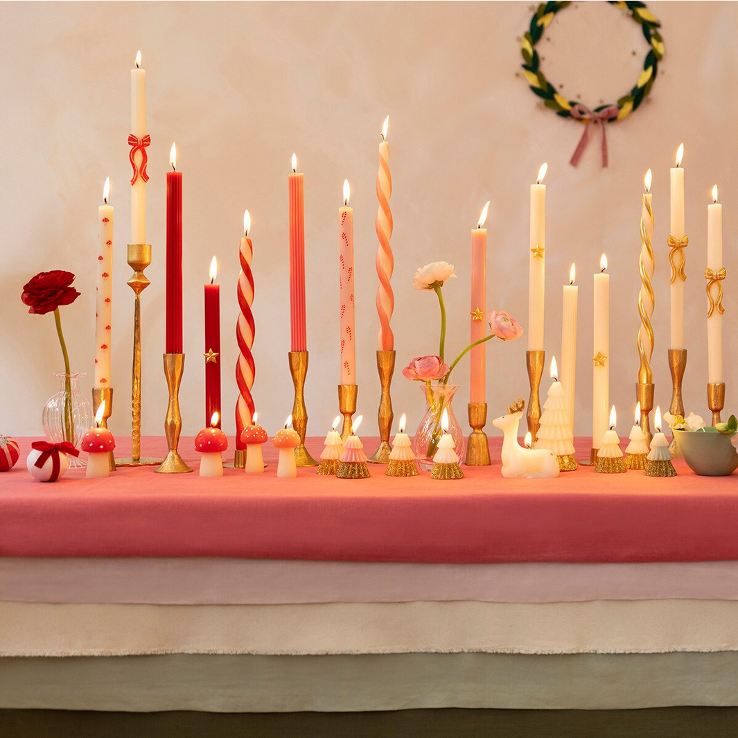 Decorative table setting with lit candles, flowers, and small decorative items on a pink tablecloth.