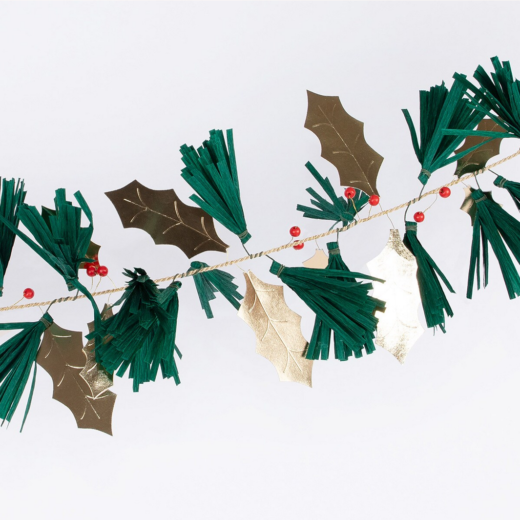 Decorative garland with green tassels, gold holly leaves, and red berries on a white background