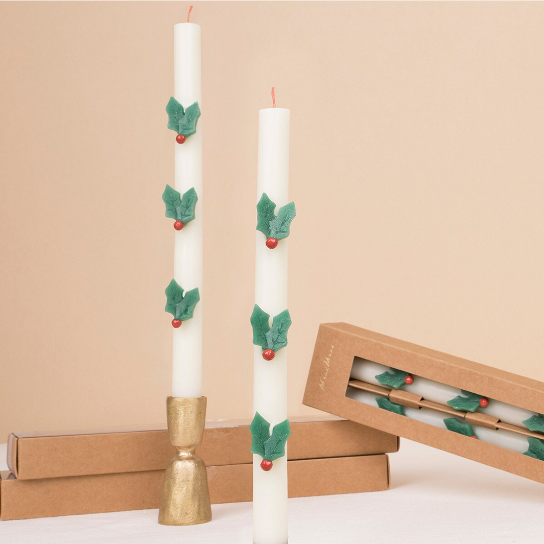 Decorative candles with holly leaves and berries on a beige background