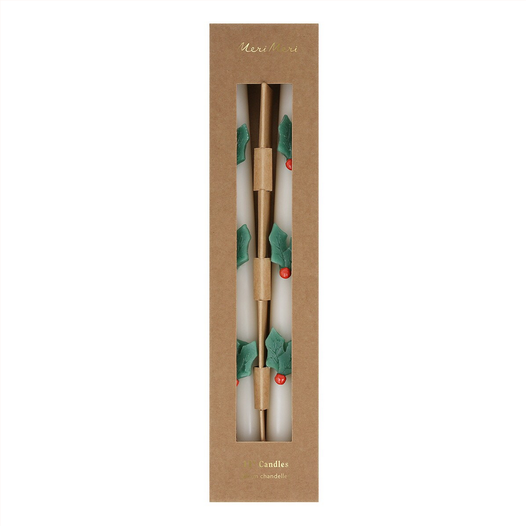 Two candles with holly design in a cardboard packaging on a white background