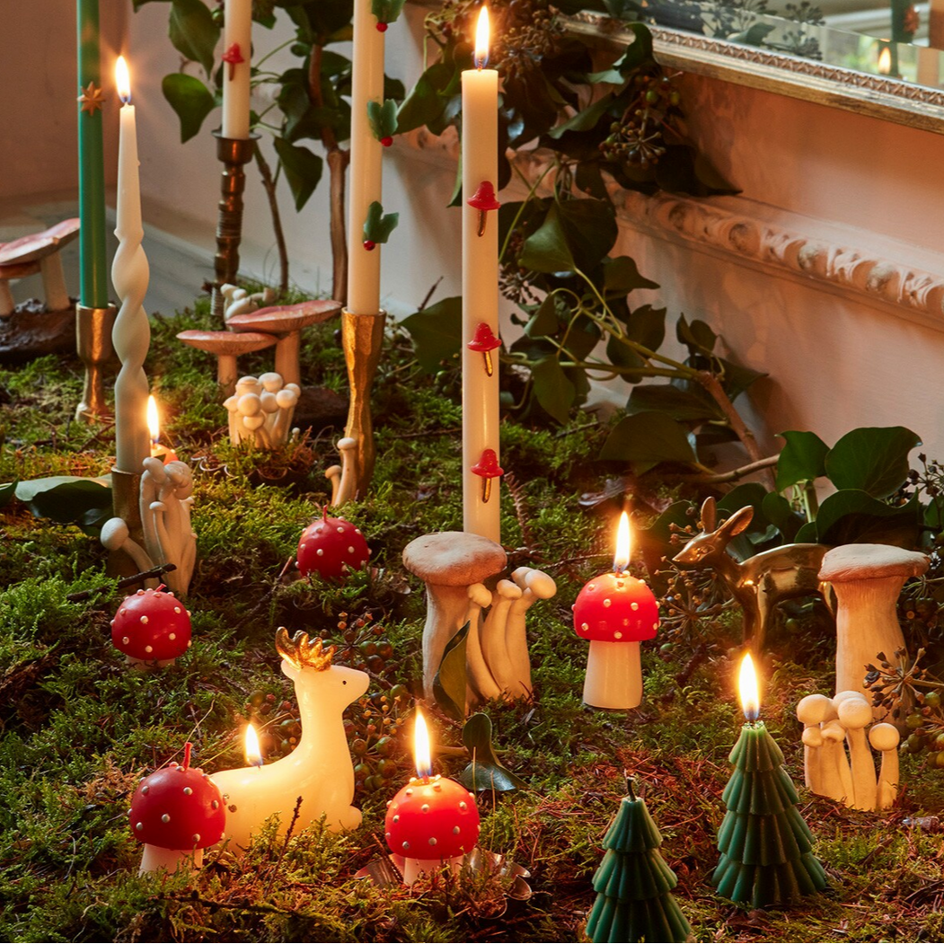 Festive arrangement with candles, mushrooms, and small deer figurines on a grassy surface.