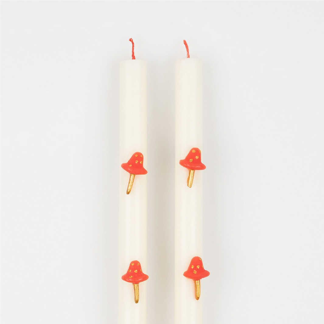 Two white candles with red mushroom-shaped candle holders on a light gray background
