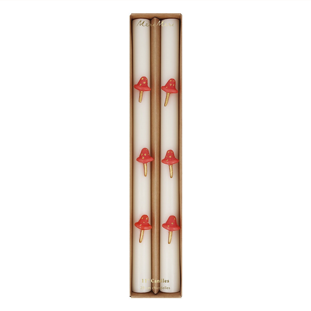 Two white candles with red mushroom designs in a cardboard box on a white background