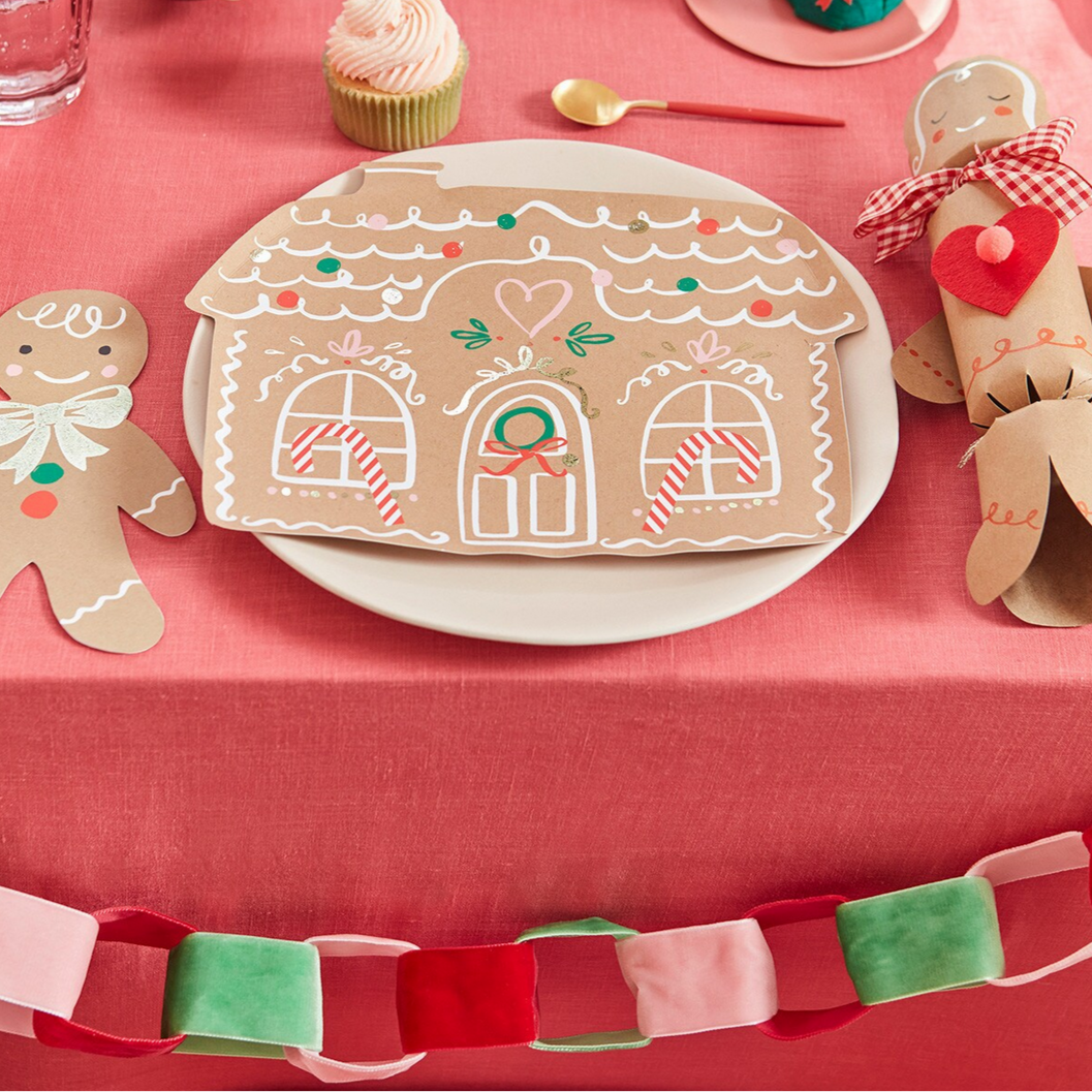 Gingerbread house cookie on a plate with decorative gingerbread men and a red tablecloth.