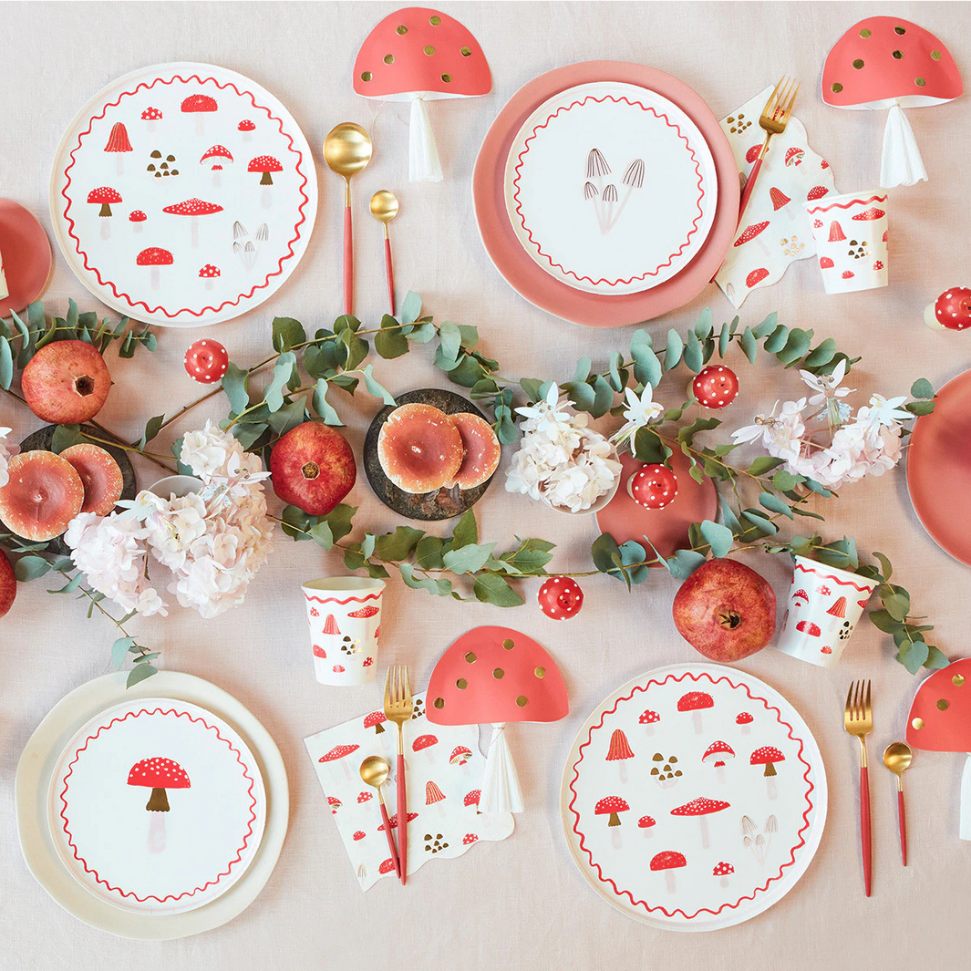 Table setting with mushroom-themed plates, cups, and cutlery on a light background.