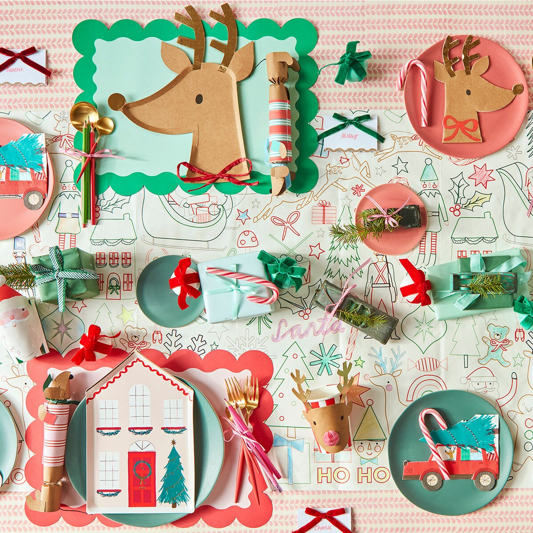 Colorful Christmas-themed tableware set with reindeer, gingerbread house, and candy cane designs on a patterned background.