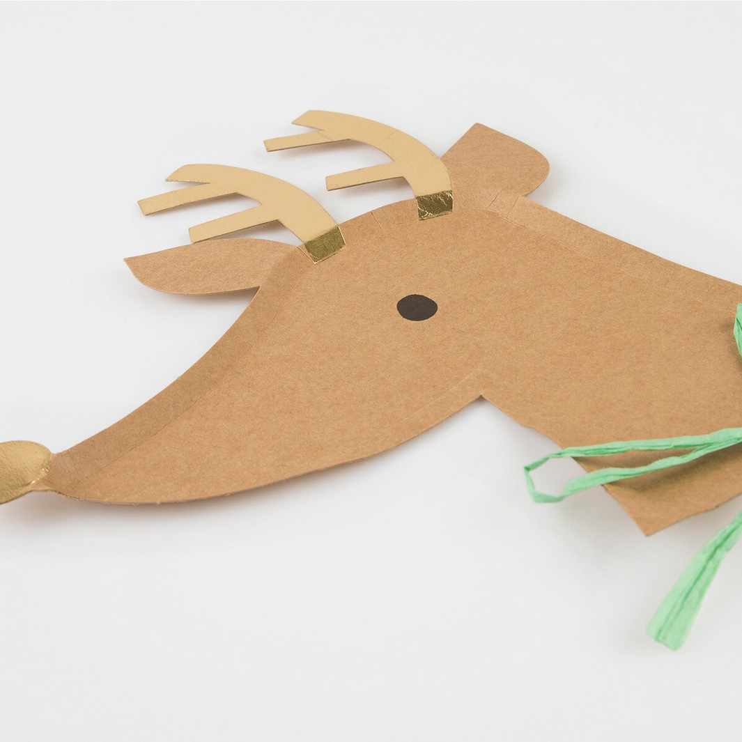 Cardboard reindeer decoration with gold antlers and green tassels on a white background