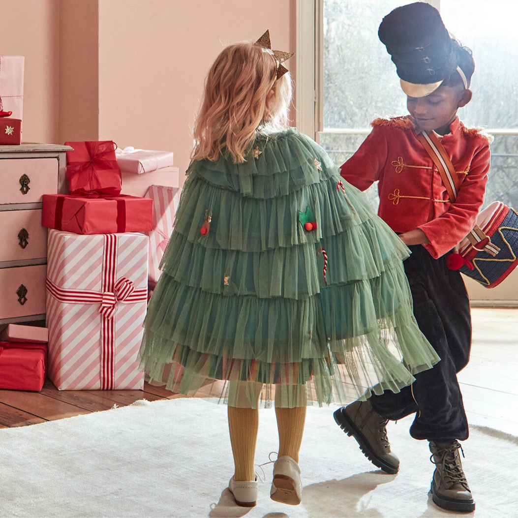 Two children in festive costumes standing in a room with Christmas decorations.