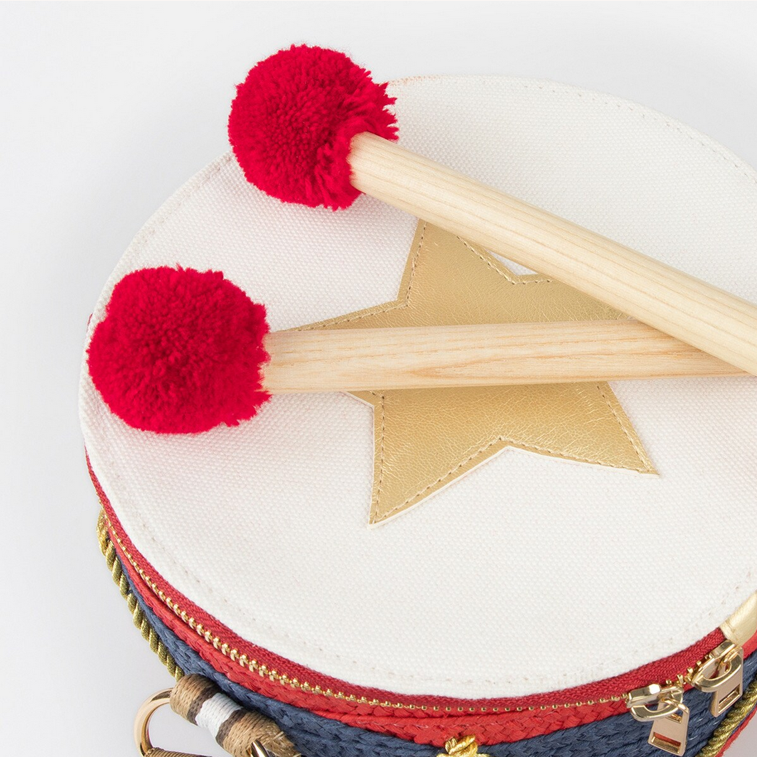 Children's drum with red pom-poms and wooden sticks on a white background