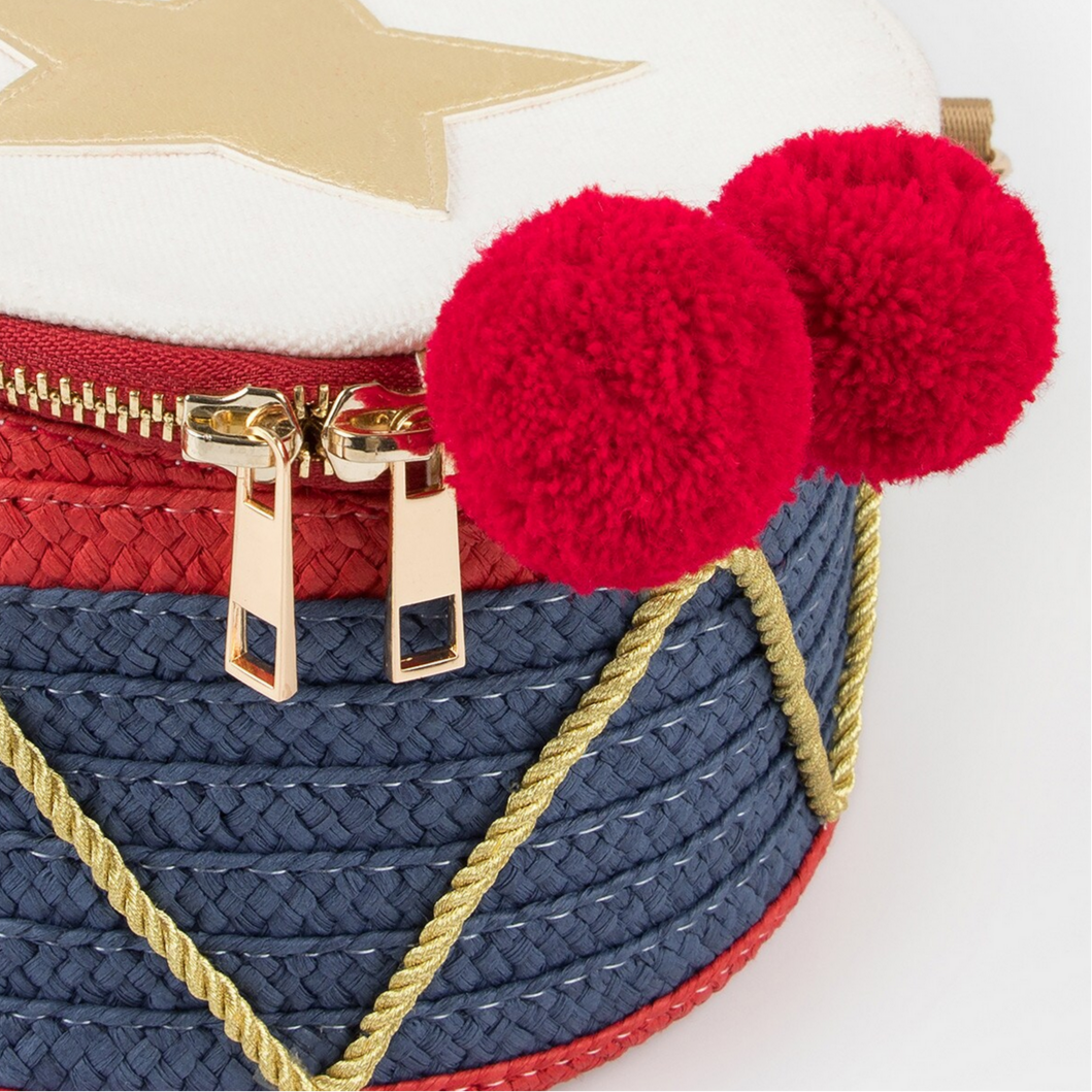 Close-up of a bag with red pom-poms and gold zipper on a white background
