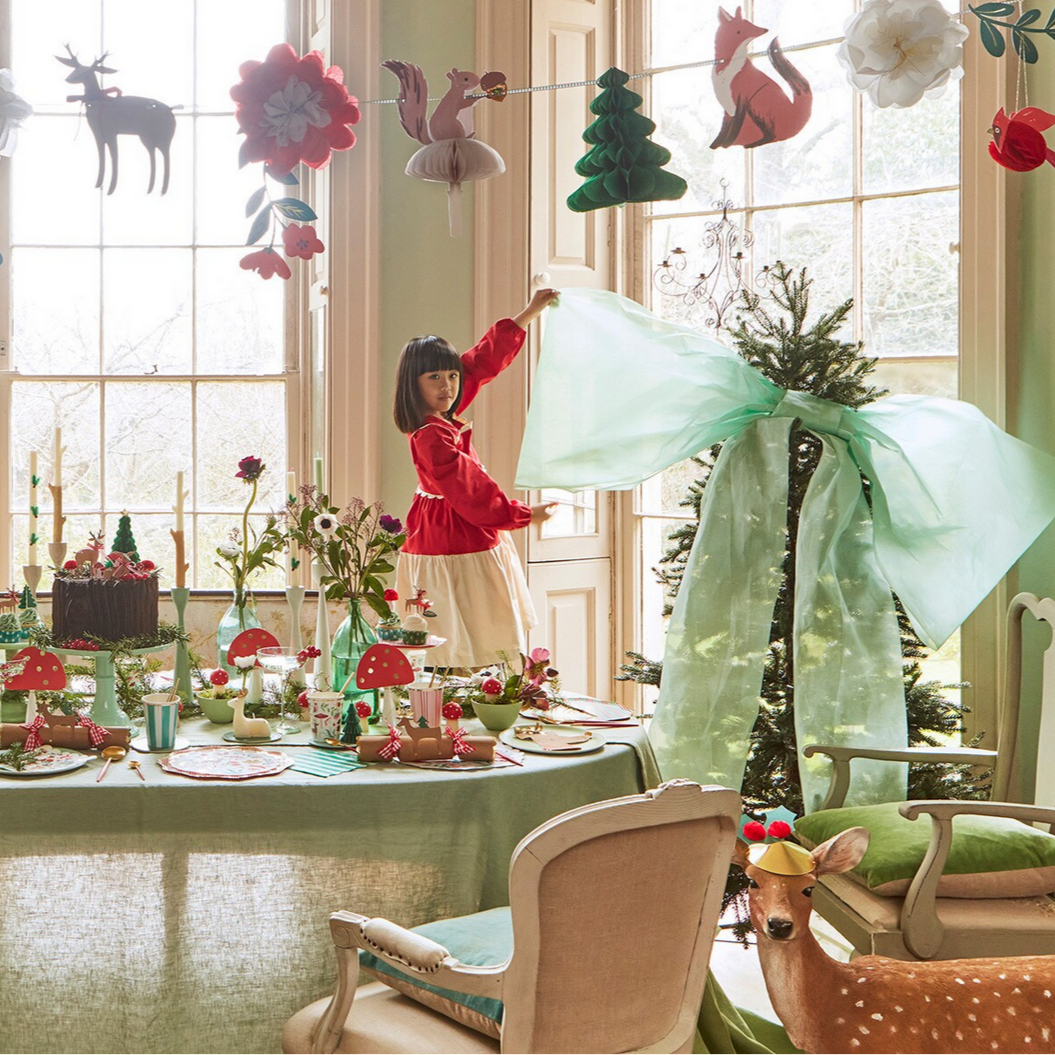 Decorative indoor setting with a child in a red dress, table with festive decorations, and hanging ornaments.