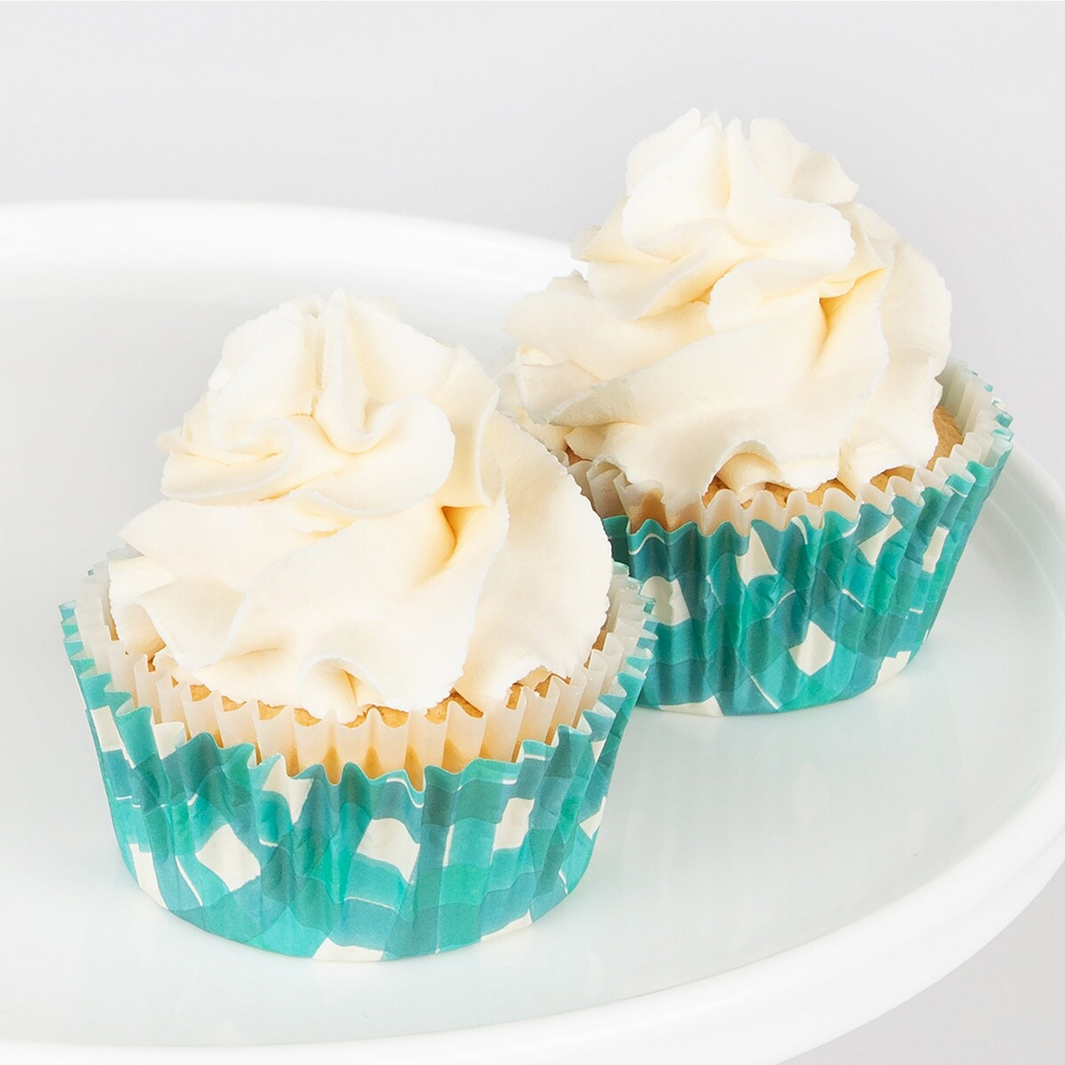 Two cupcakes with white frosting in teal and white striped liners on a white plate.