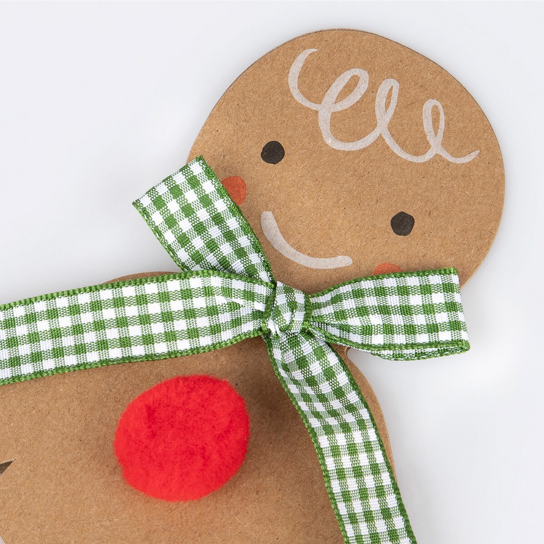 Gingerbread man decoration with a green and white checkered ribbon on a white background
