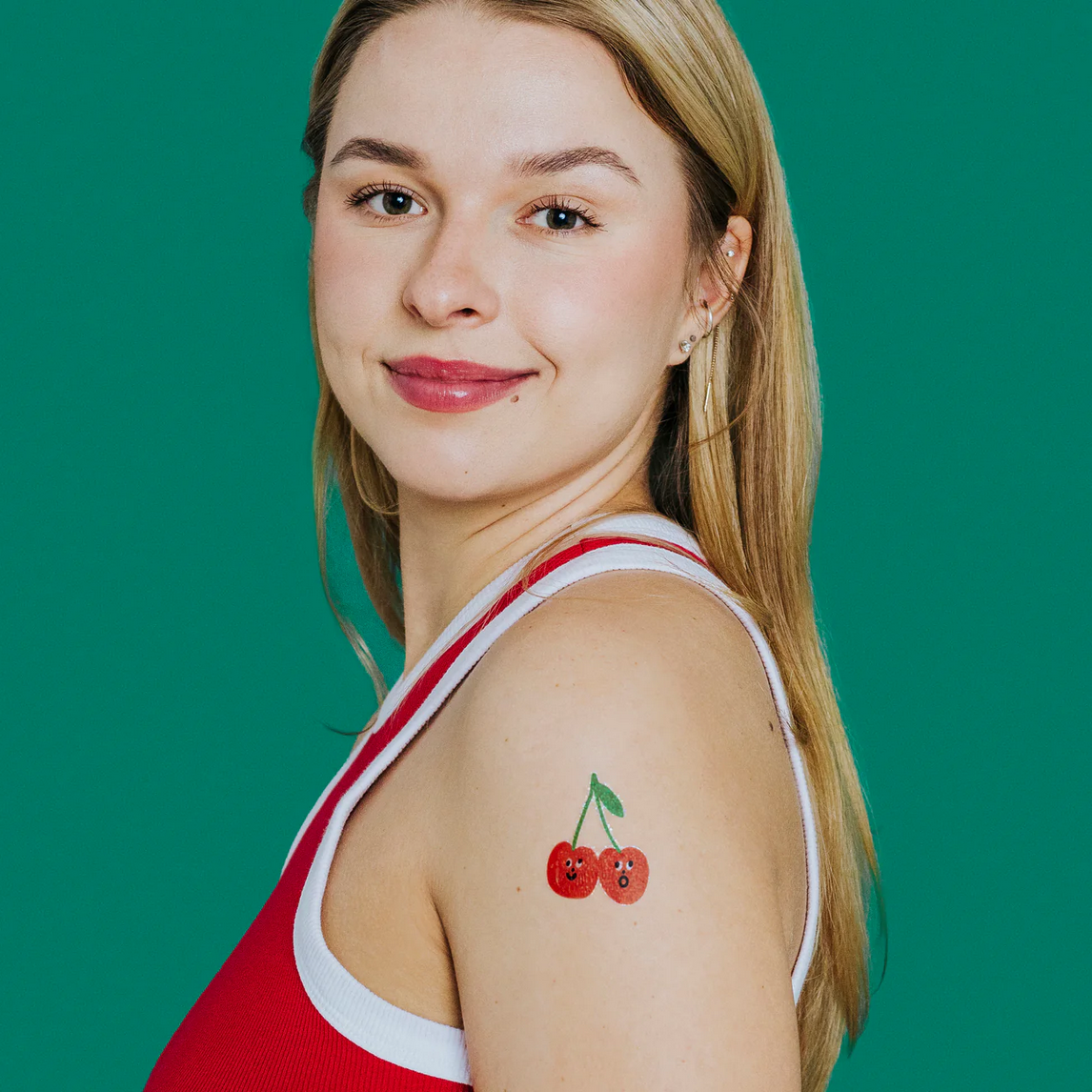 Woman with a cherry tattoo on her shoulder against a green background