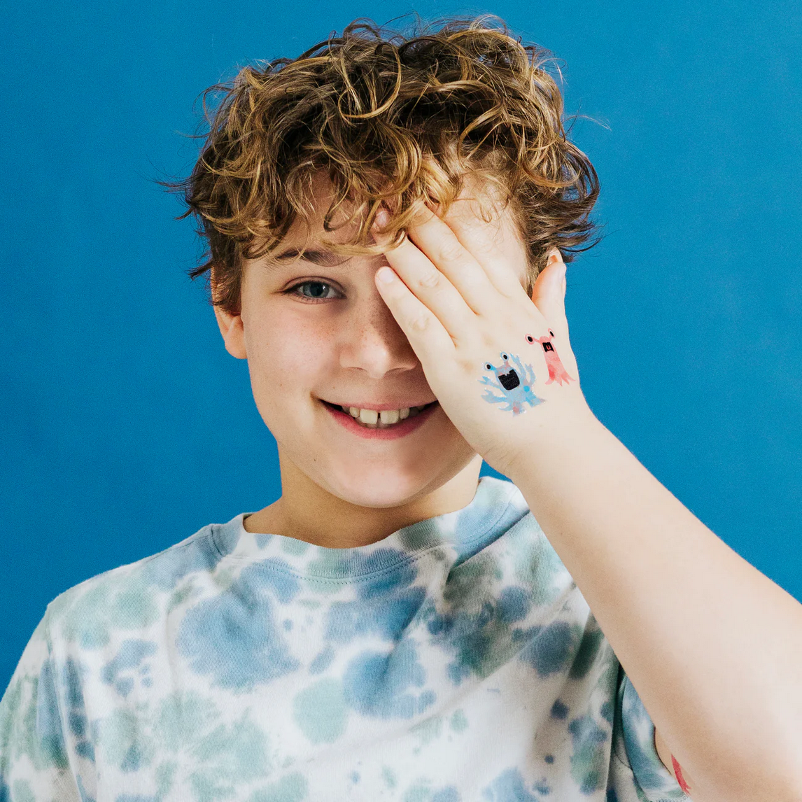 Young boy with colorful temporary tattoos on his arm against a blue background