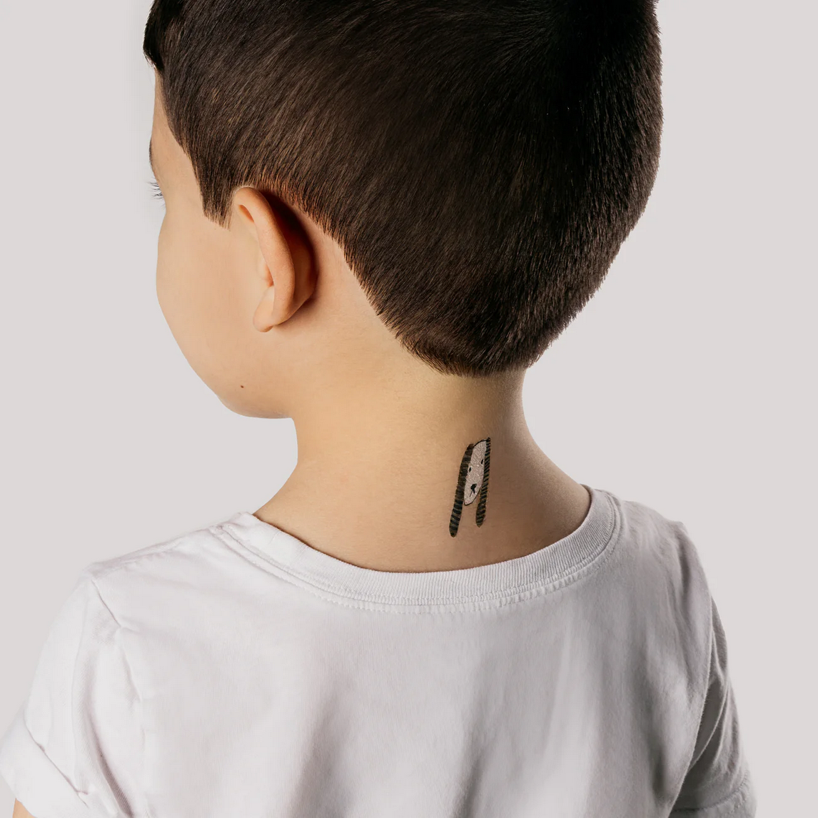 Person wearing a white shirt with a small tattoo on the neck against a plain background