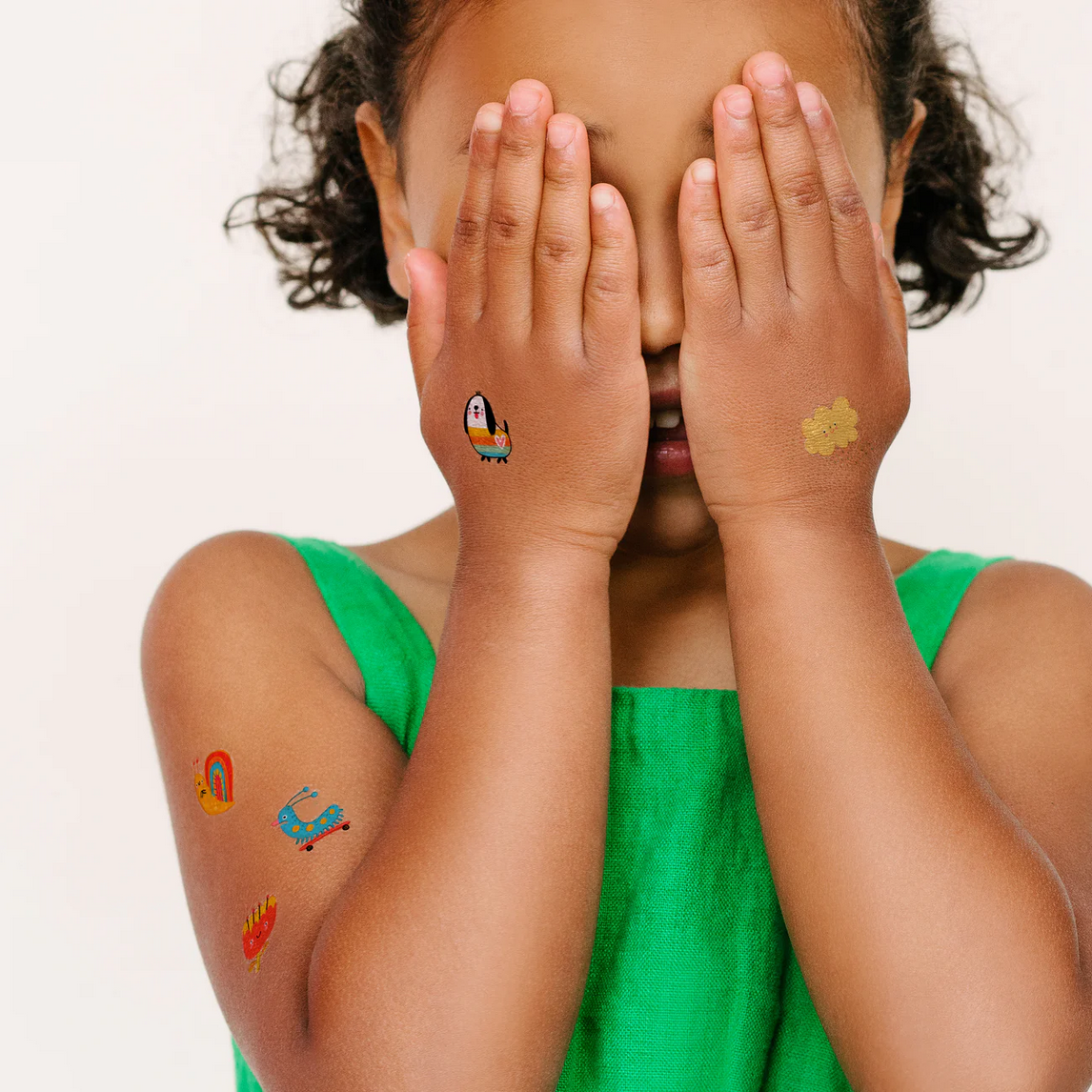 Child with temporary tattoos on arms and hands, wearing a green dress.