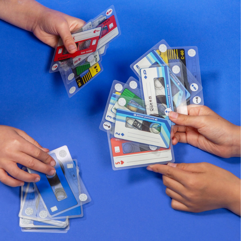 Hands playing with cassette tape-themed cards on a blue background