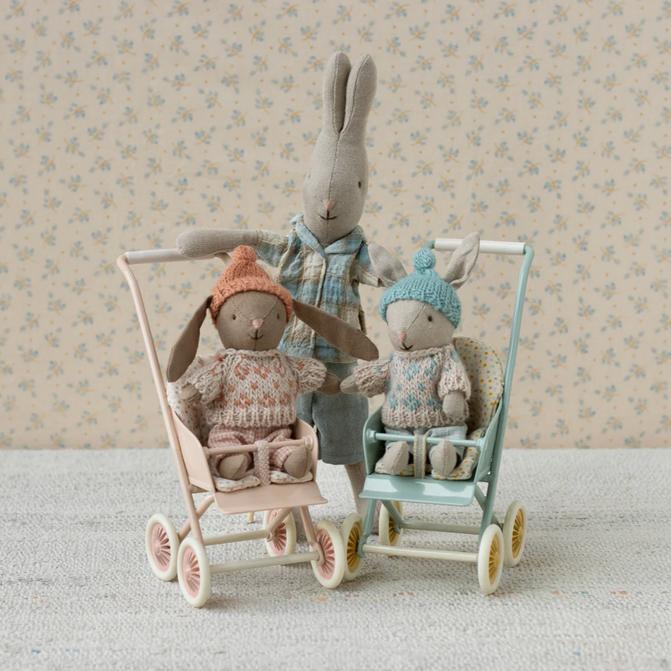 Two stuffed animals in a toy stroller against a floral wallpaper background