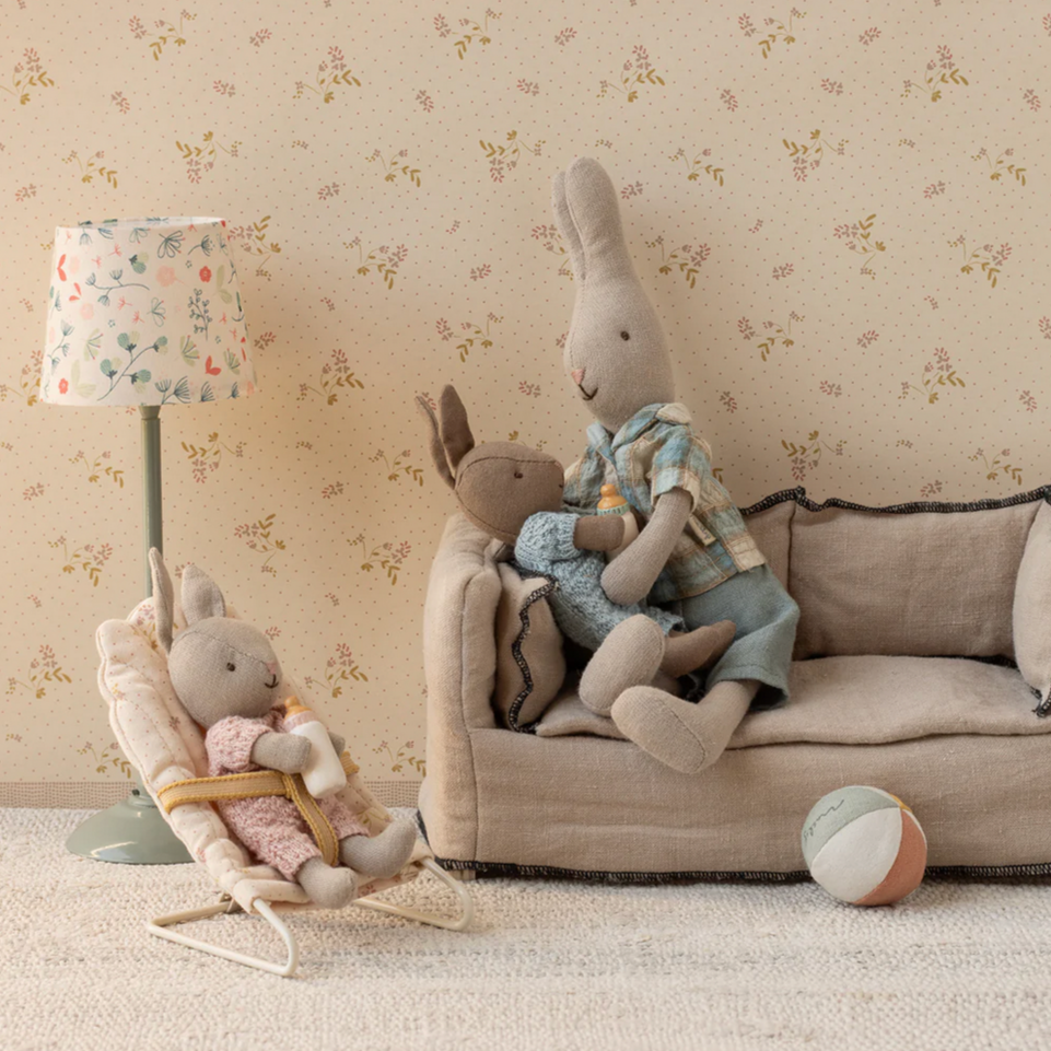 Children's room with plush toys on a sofa and chair against a floral wallpaper background.