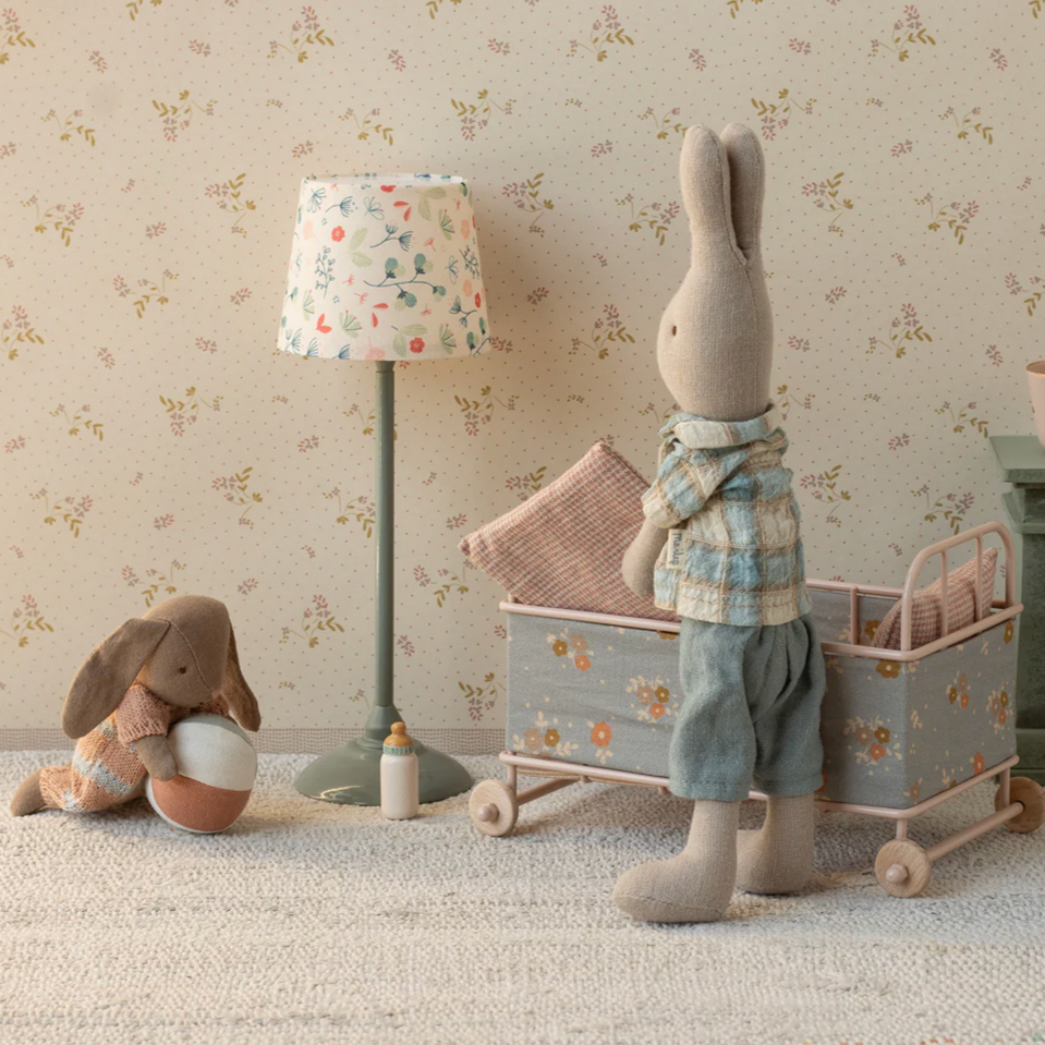 Children's room with toys, a lamp, and a crib against a floral wallpaper.