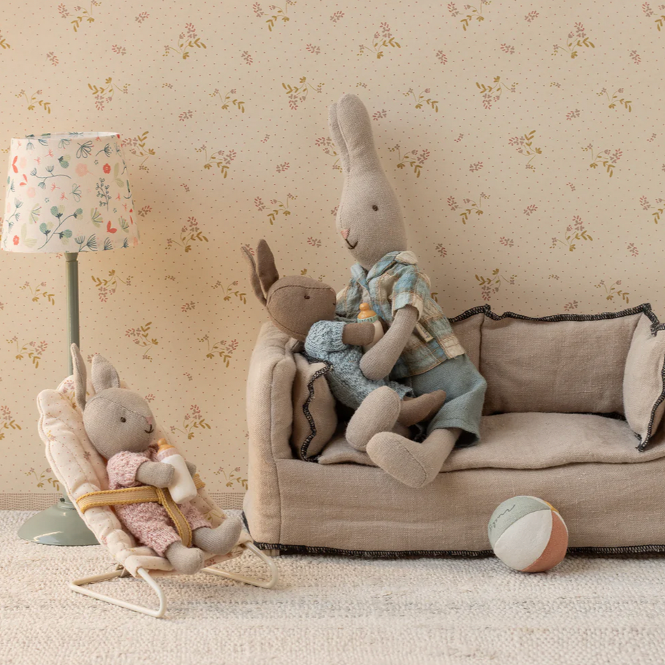 Children's room with plush toys on a sofa and chair against a floral wallpaper.