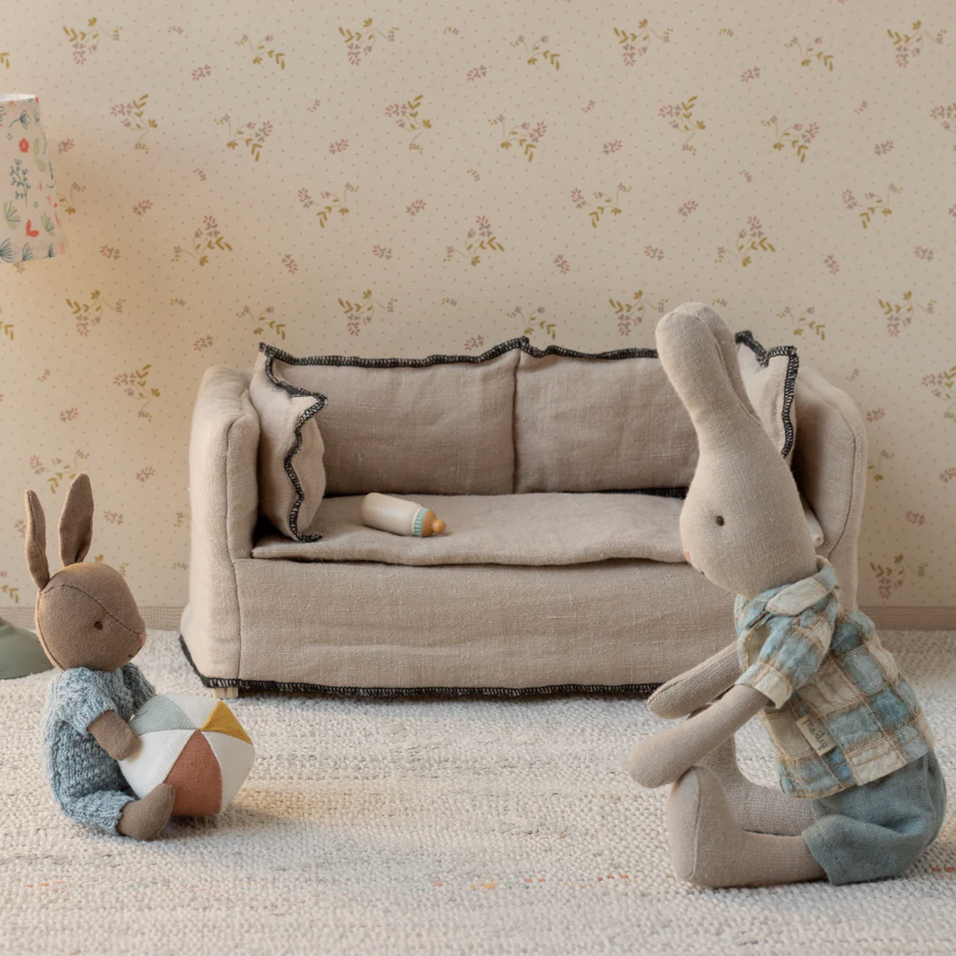 Two stuffed rabbit toys in a room with a sofa and lamp.