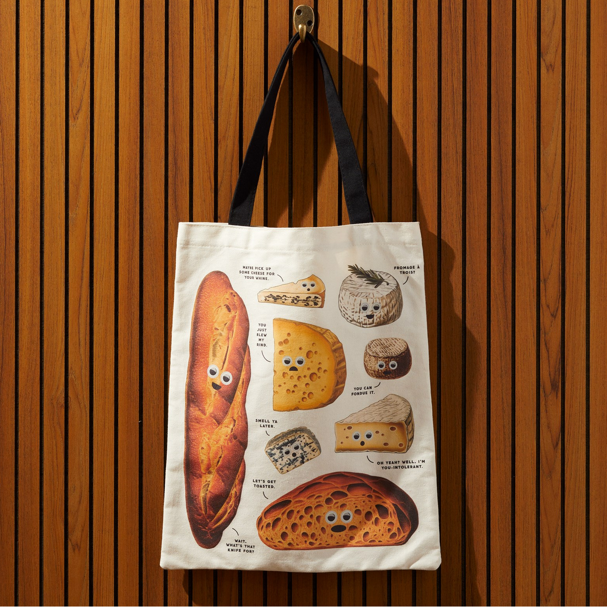Tote bag with bread and cheese illustrations hanging on a wooden wall