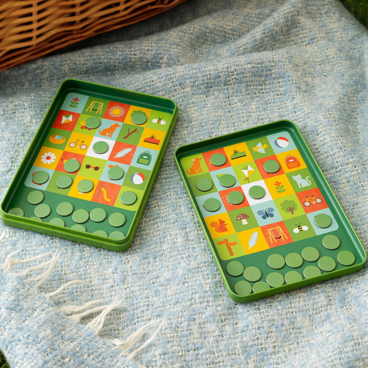Two green board games with colorful tiles on a textured fabric surface.