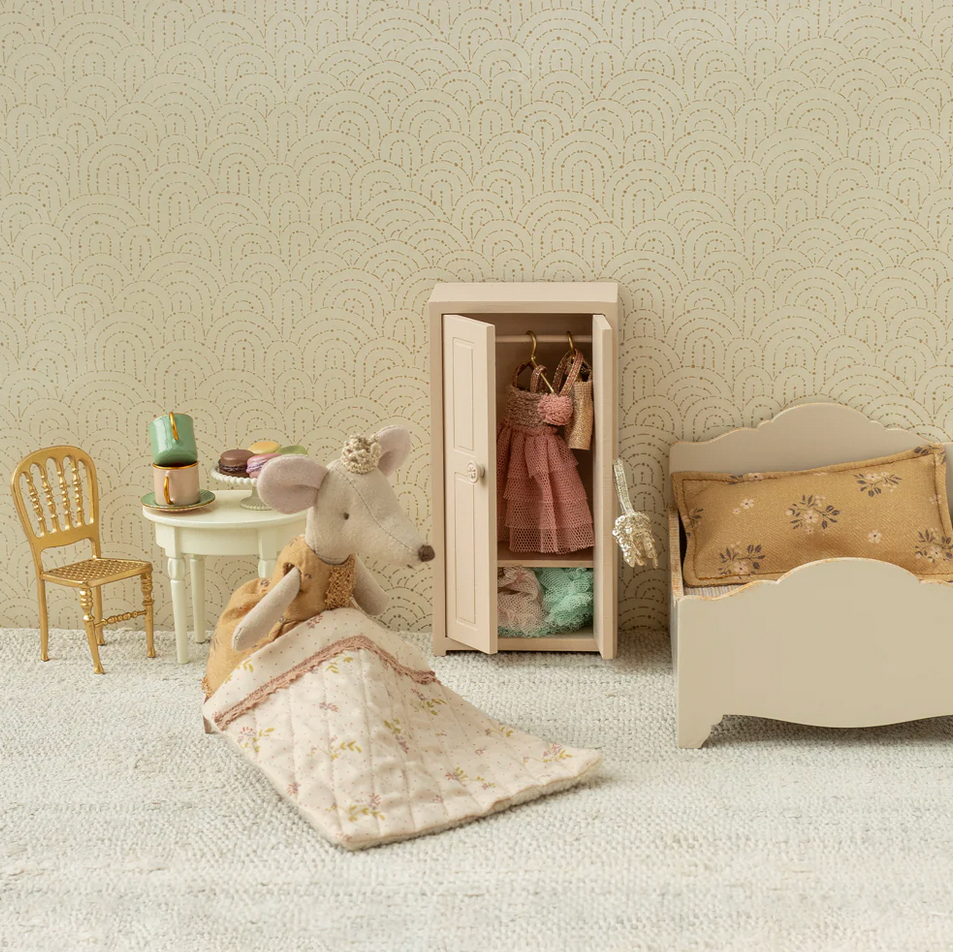 Miniature bedroom set with bed, chair, and wardrobe against a patterned wall.