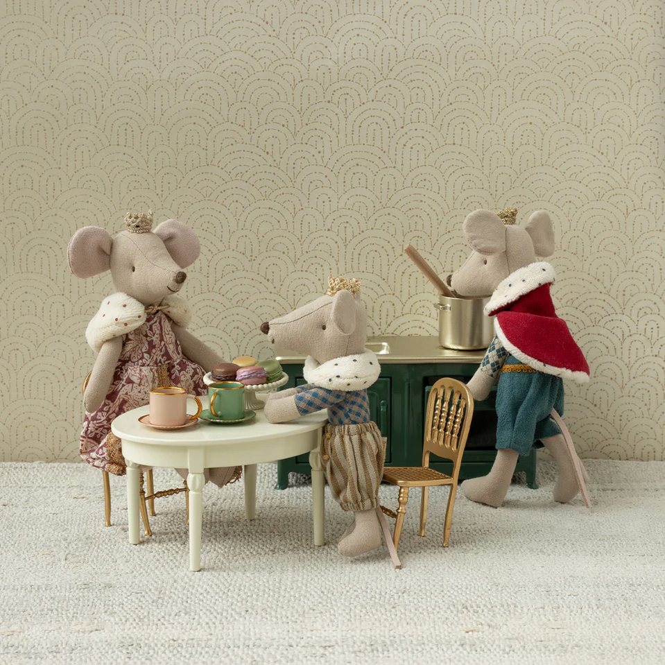 Three toy mice with a tea set on a small table against a patterned wall.