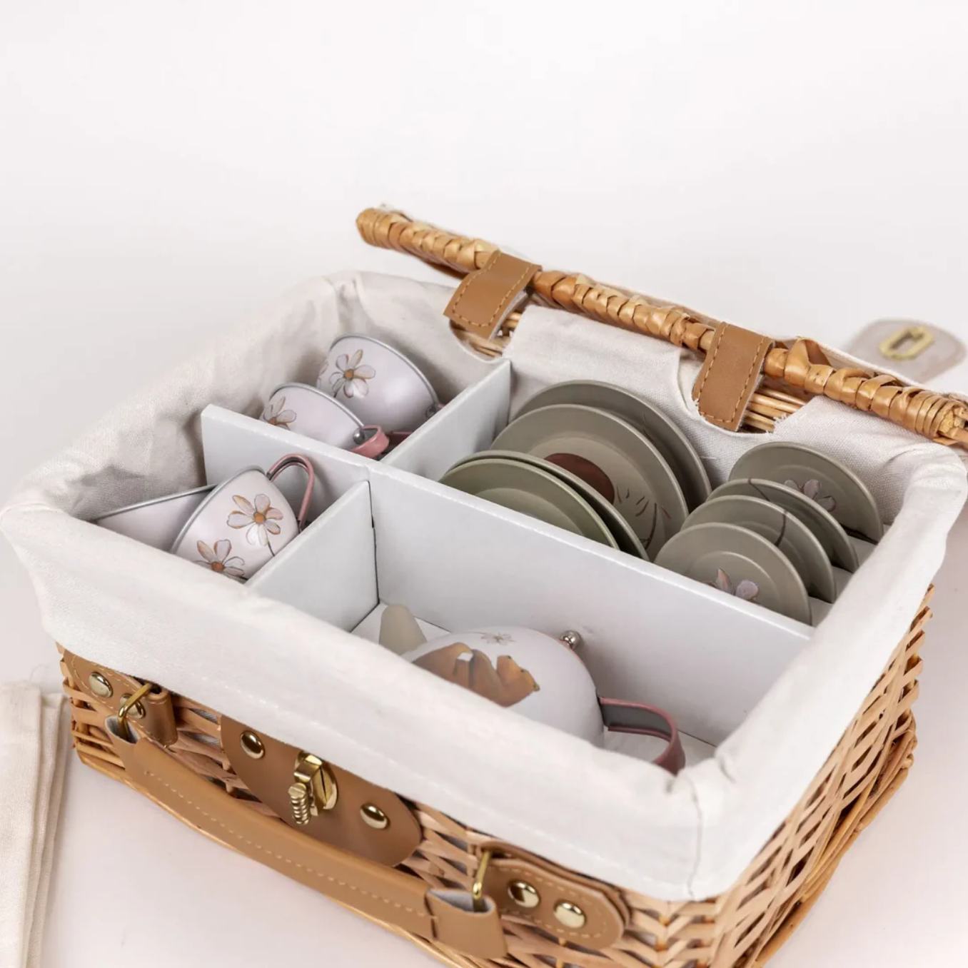 Wicker picnic basket with organized compartments containing cups and saucers on a white background