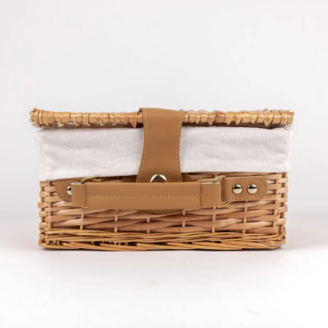 Wicker picnic basket with a white liner and brown leather handles on a white background