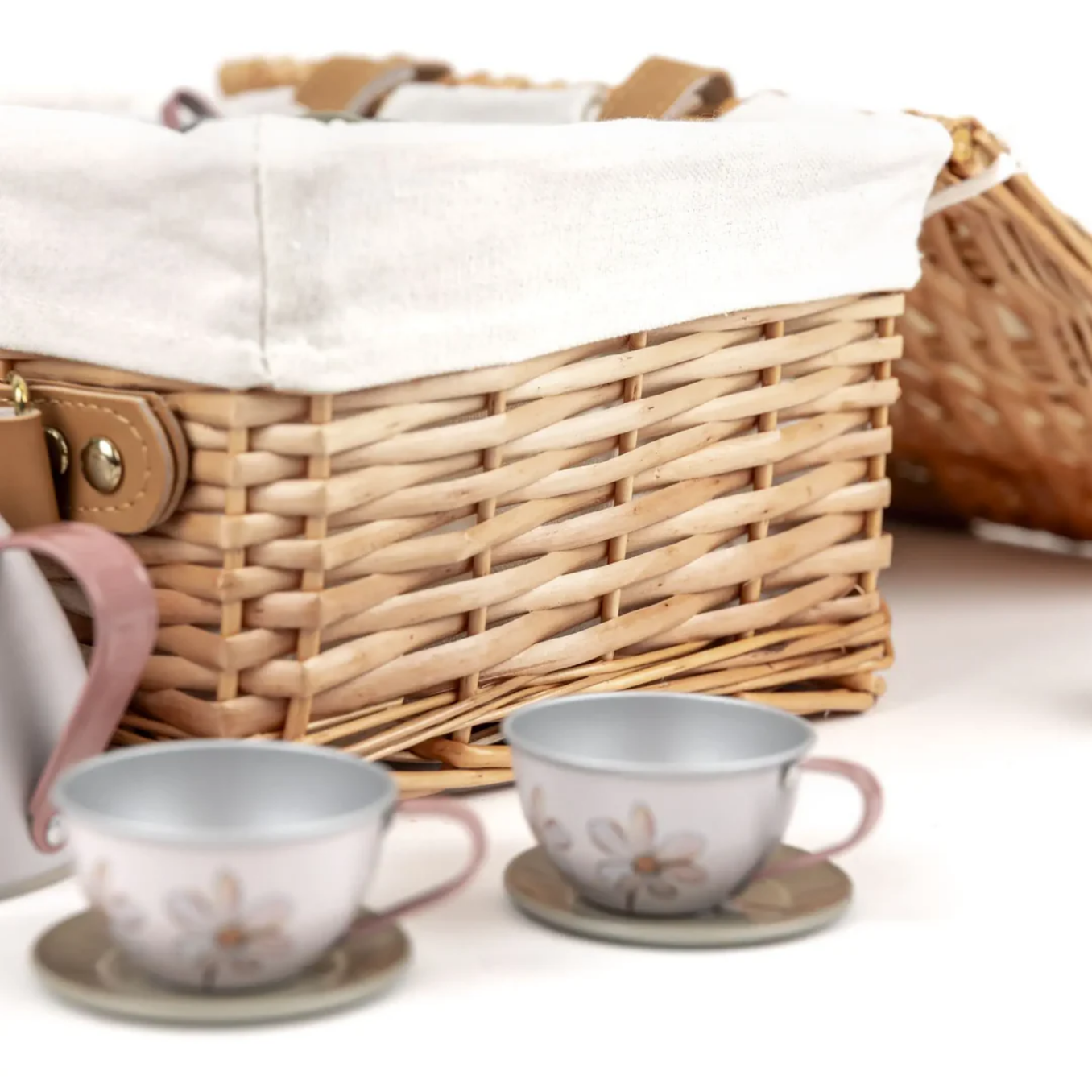 Wicker picnic basket with two tea cups and saucers on a white background