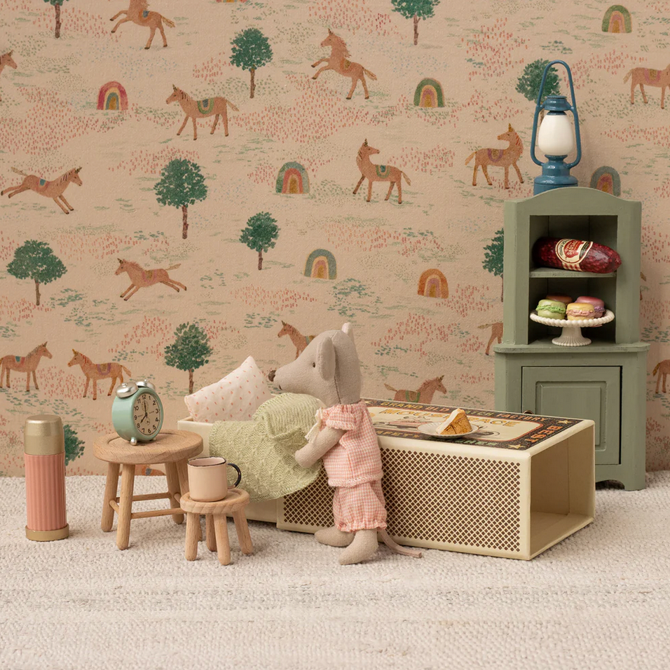 Children's room with toy furniture and decorative items against a wallpapered wall.