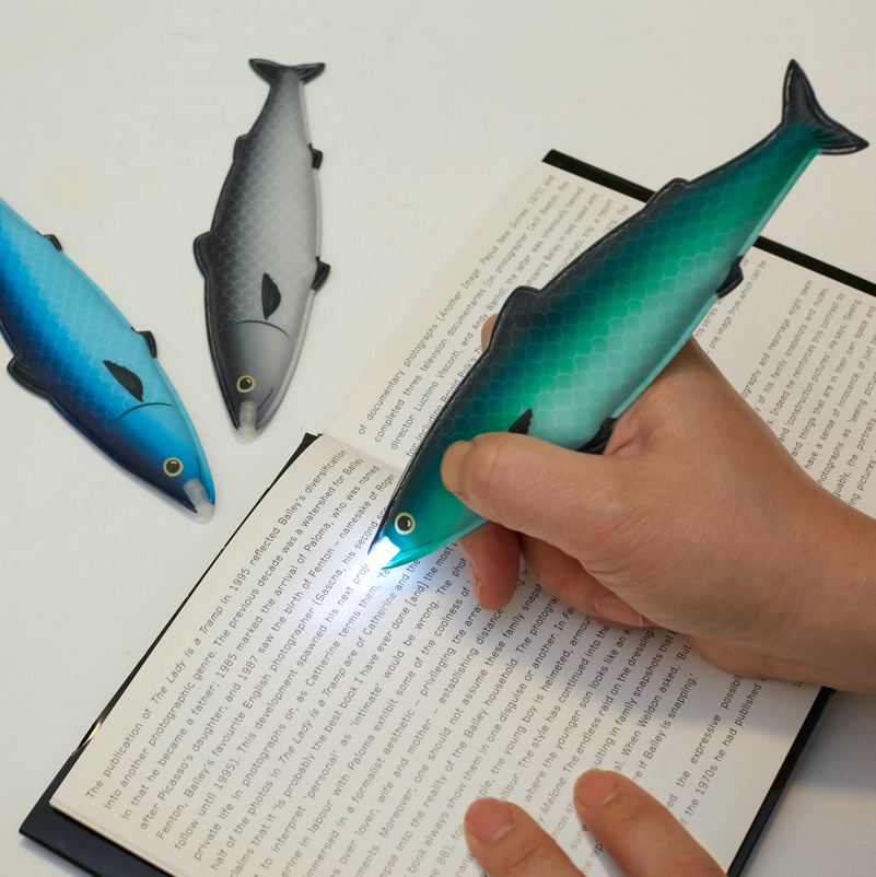 Fish-shaped flashlight held over an open book with other fish-shaped flashlights in the background.