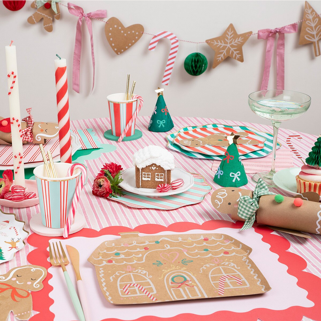 Christmas-themed table setting with gingerbread house placemats, candy canes, and festive decorations.