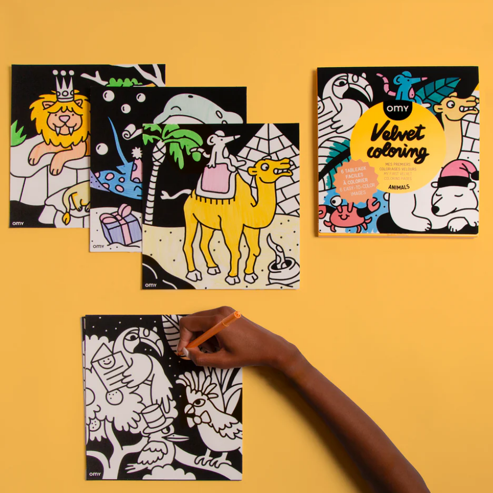 Coloring books with animal illustrations on a yellow background, one book open with a hand coloring.