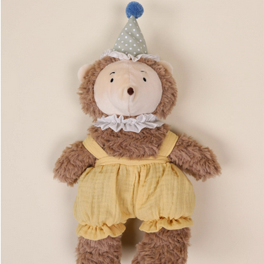 Plush toy hedgehog in a yellow outfit with a blue party hat on a beige background